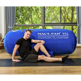 A person sitting next to a Macy-Pan ST901 soft capsule hyperbaric chamber showing its large 88 inch length.